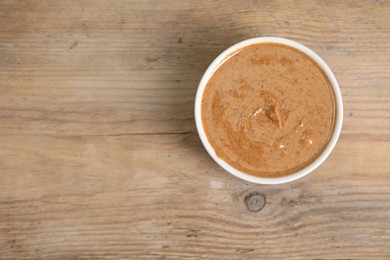 Photo of Delicious nut butter in bowl on wooden table, top view. Space for text