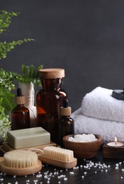 Photo of Spa composition. Brushes, soap bar, bottles and sea salt on black table