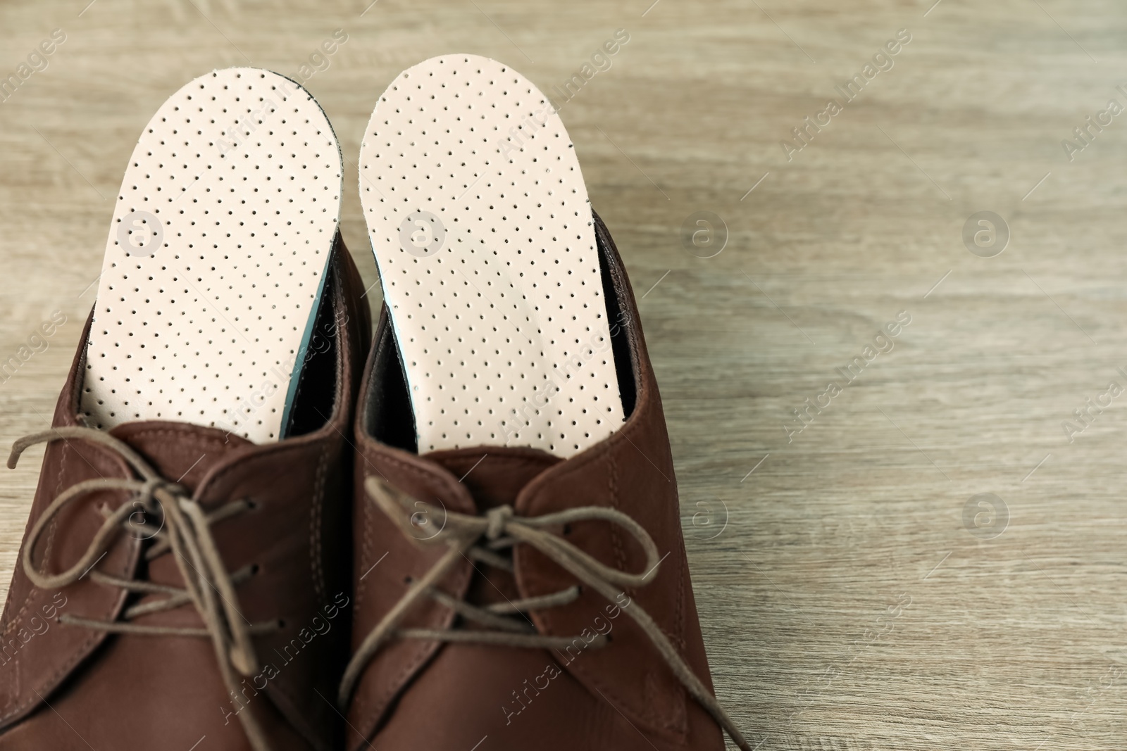 Photo of Orthopedic insoles in shoes on floor, closeup. Space for text