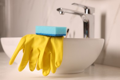 Photo of Sponge and rubber gloves on bathroom sink indoors, closeup