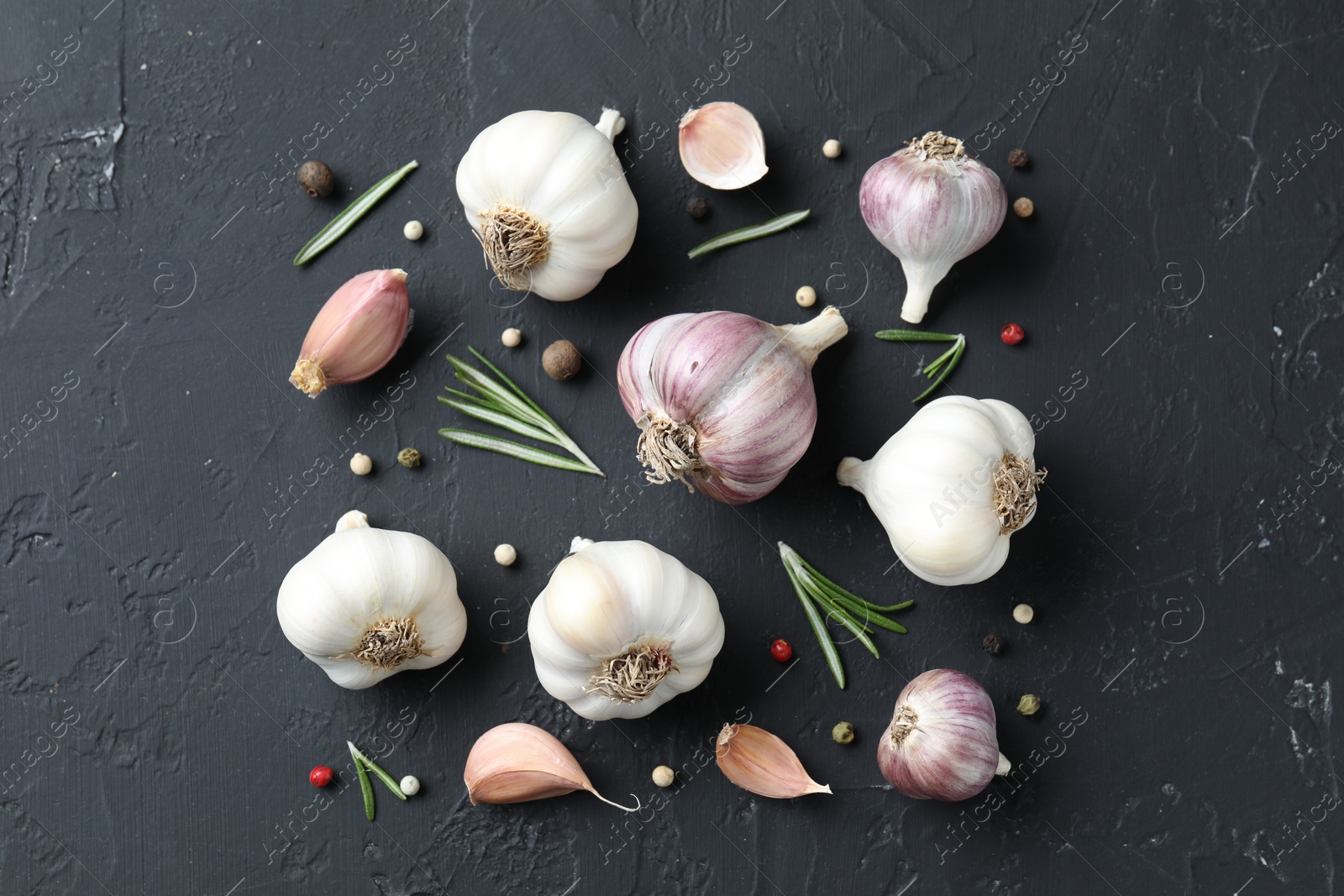 Photo of Fresh garlic, rosemary and peppercorns on dark textured table, flat lay