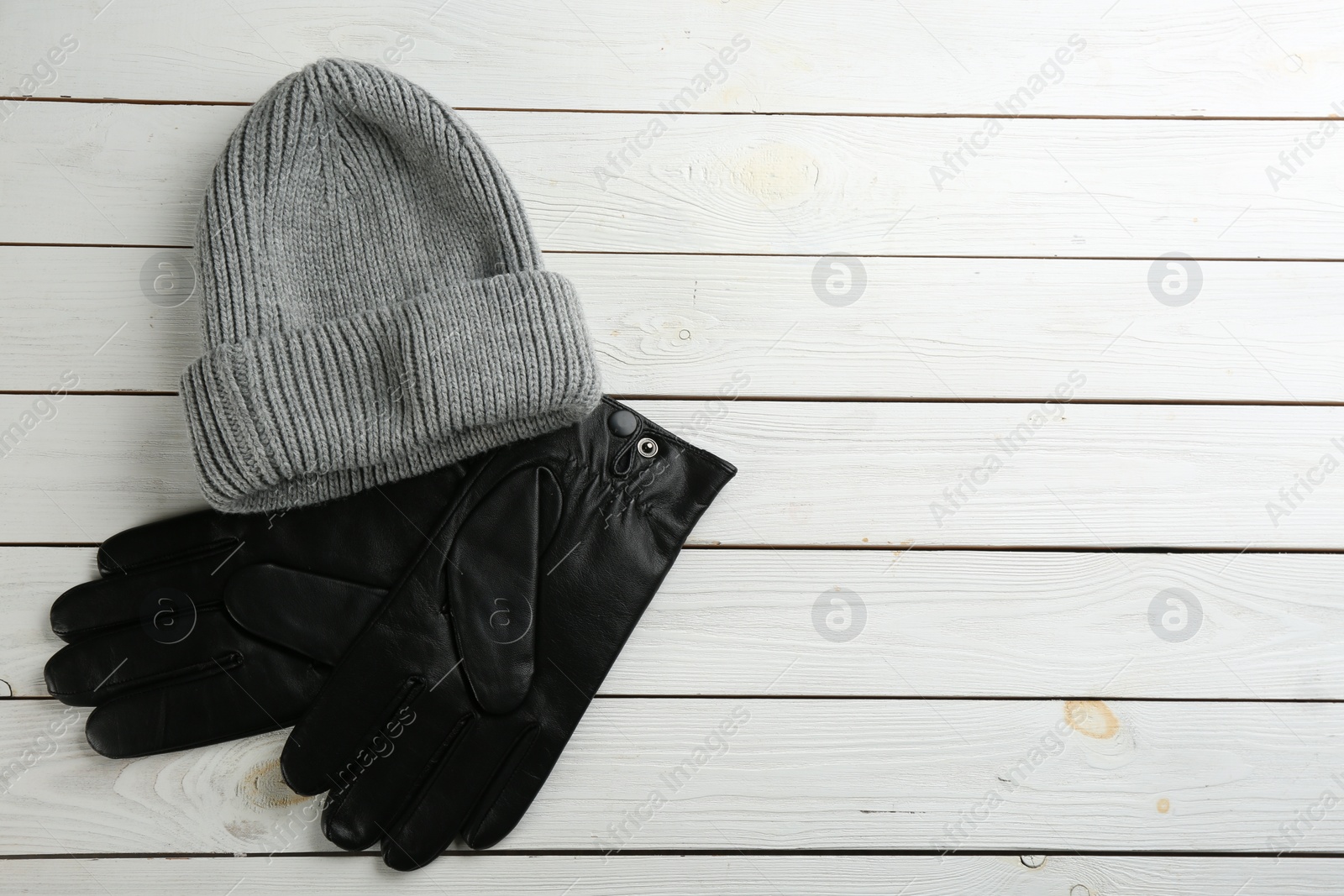 Photo of Stylish black leather gloves and hat on white wooden background, flat lay. Space for text