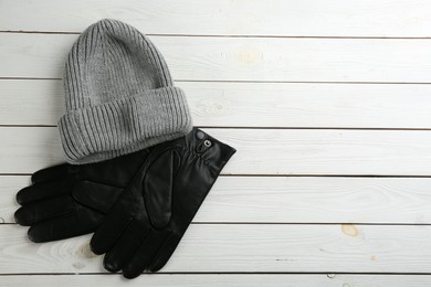 Photo of Stylish black leather gloves and hat on white wooden background, flat lay. Space for text