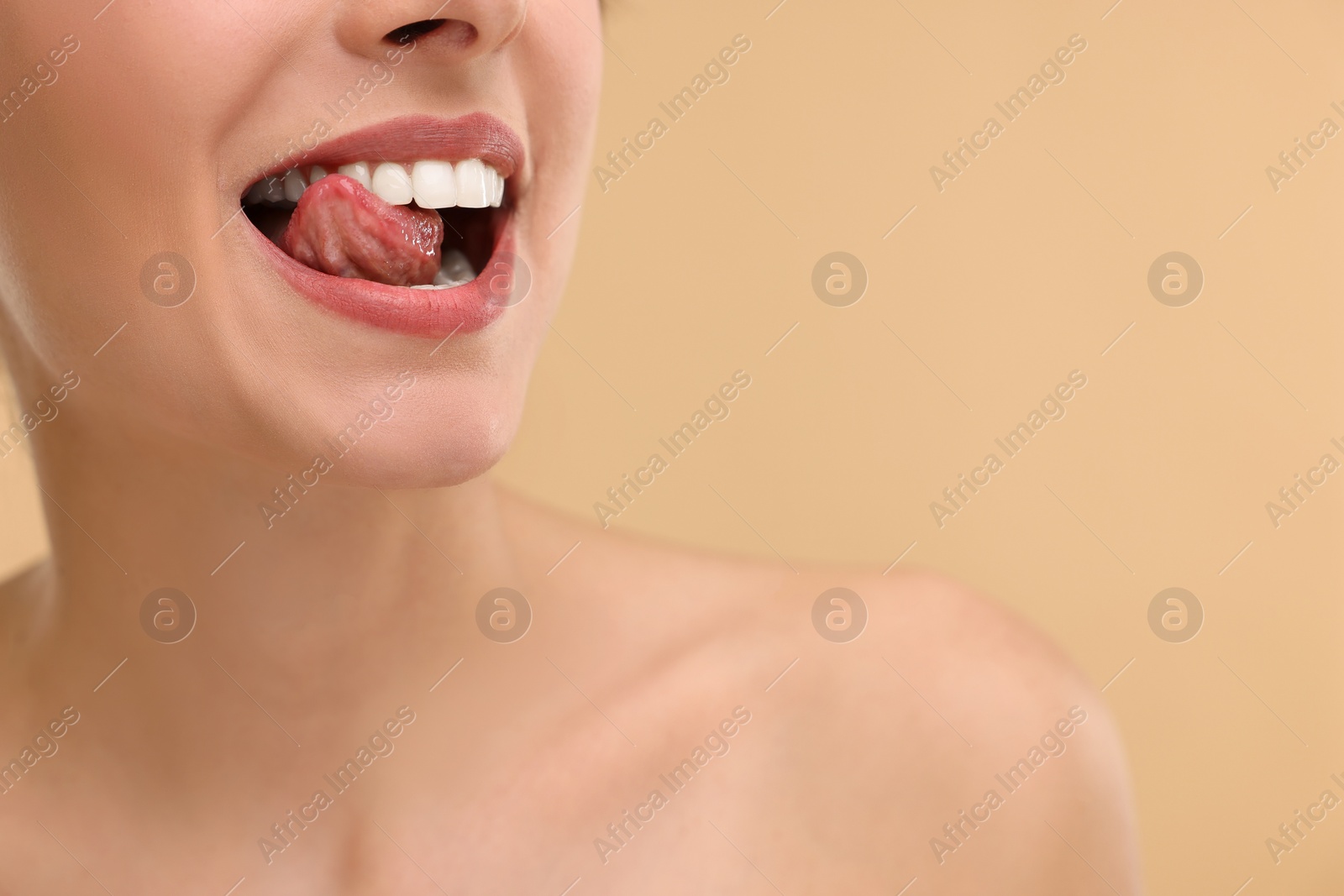 Photo of Woman with beautiful lips licking her teeth on beige background, closeup. Space for text