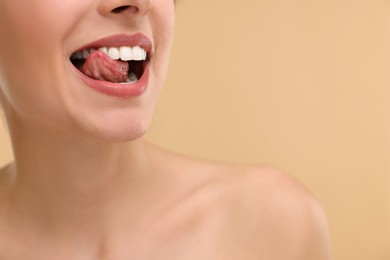Woman with beautiful lips licking her teeth on beige background, closeup. Space for text