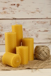 Photo of Stylish elegant beeswax candles and jute twine on white wooden table