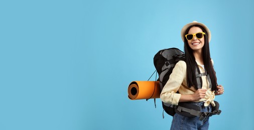 Photo of Happy female tourist with backpack on light blue background. Space for text