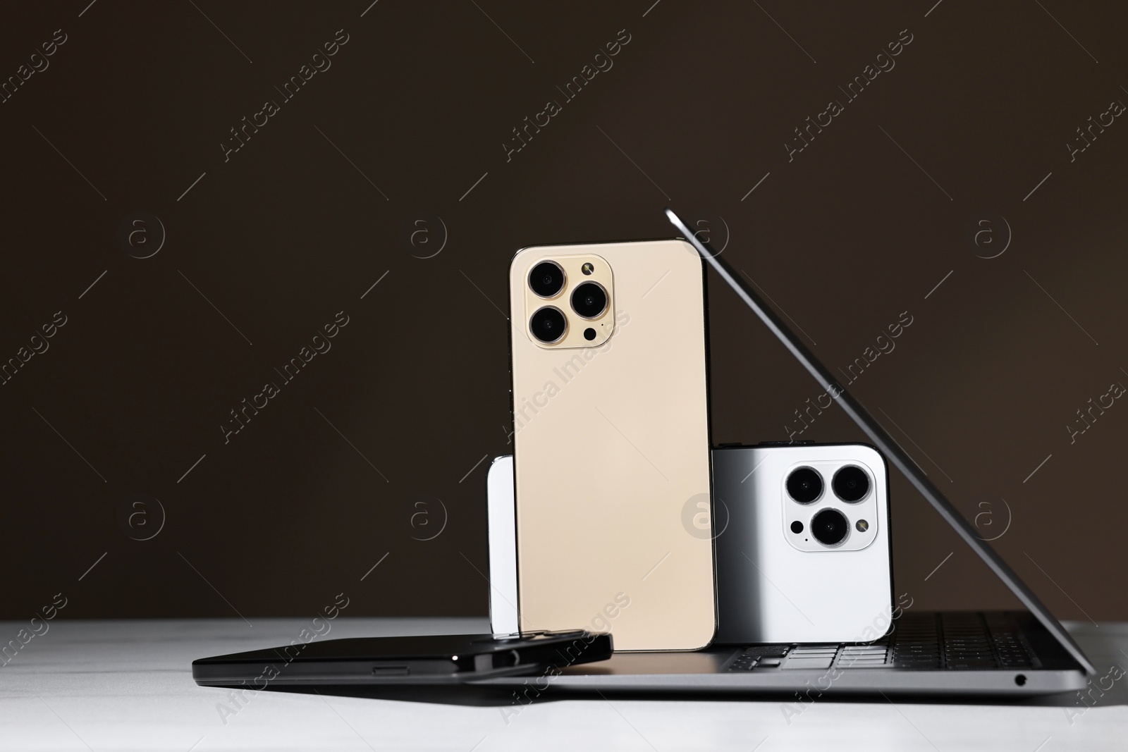 Photo of Modern laptop and smartphones on white table against brown background