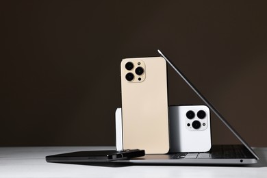 Photo of Modern laptop and smartphones on white table against brown background