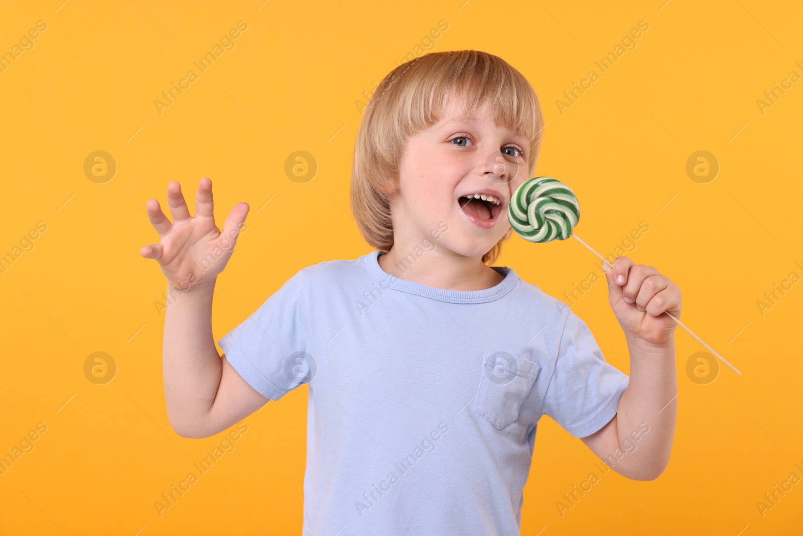 Photo of Happy little boy with bright lollipop swirl on orange background