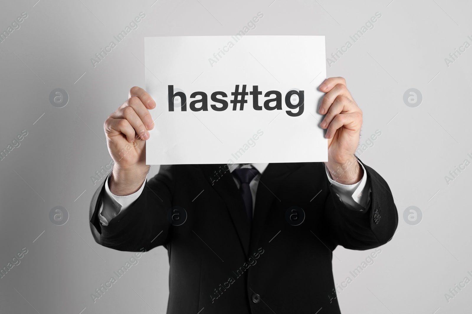 Photo of Man hiding face behind sheet of paper with symbol and word Hashtag on light background