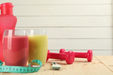 Tasty shakes, measuring tape, dumbbells and powder on wooden table, space for text. Weight loss