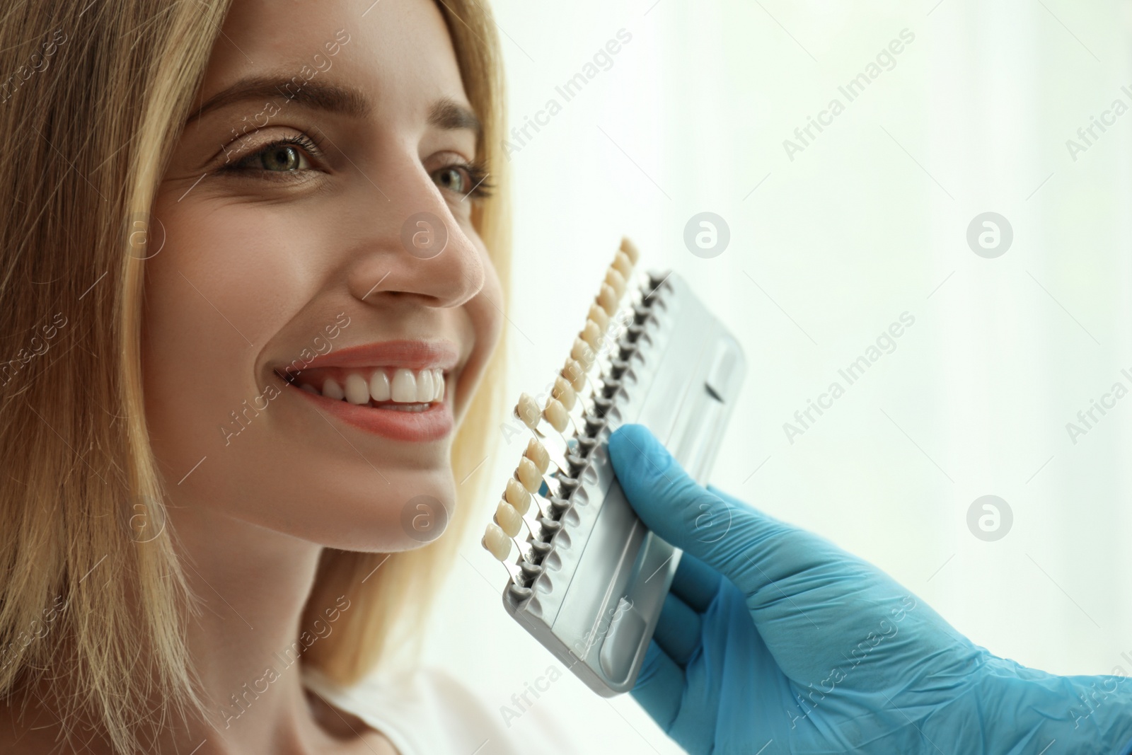 Photo of Doctor matching patient's teeth color with palette on light background, closeup. Cosmetic dentistry