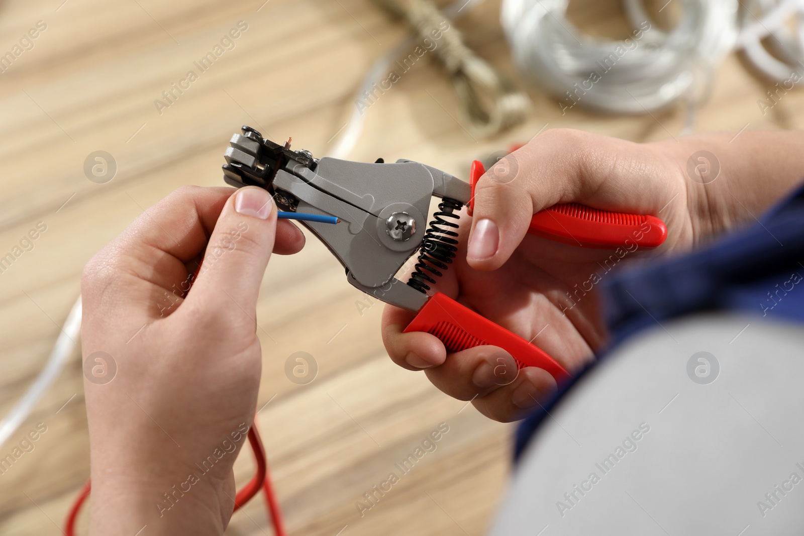 Photo of Professional electrician stripping wiring at wooden table, above view