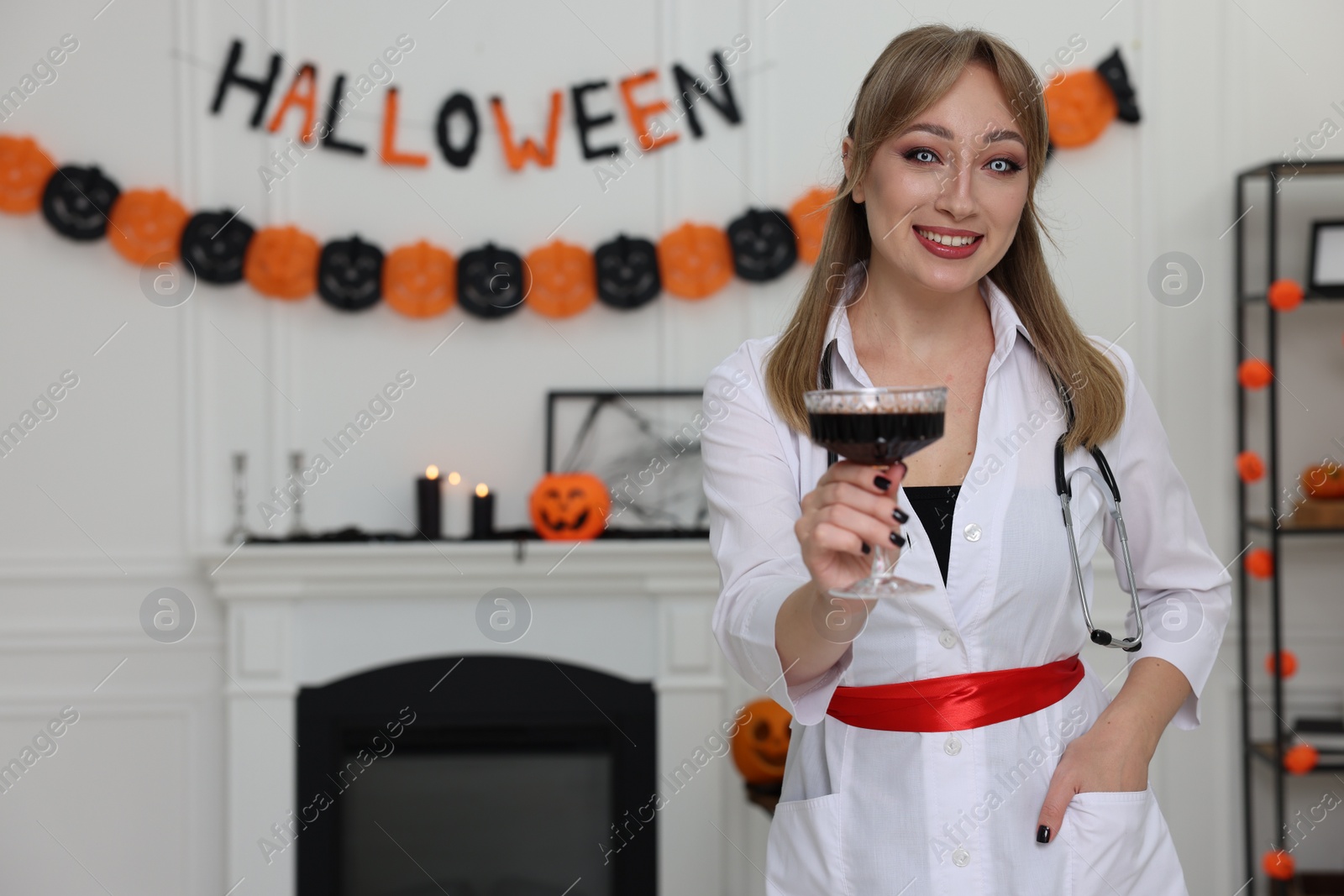 Photo of Happy woman in scary nurse costume with glass of wine indoors, space for text. Halloween celebration