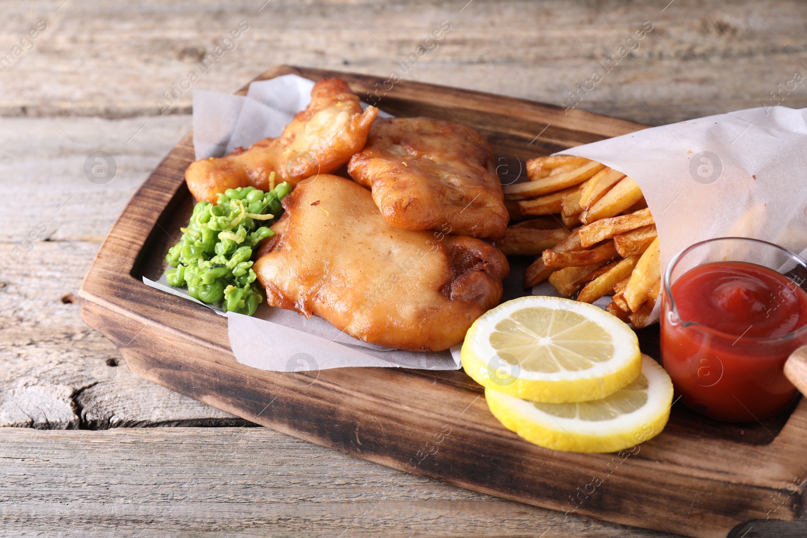 Photo of Tasty fish, chips, sauce and peas on wooden table, closeup