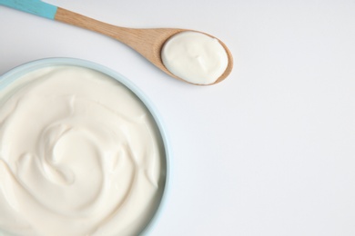 Photo of Bowl of sour cream and wooden spoon on white background, top view