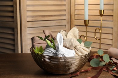 Photo of Furoshiki technique. Gifts packed in different fabrics, flowers, eucalyptus leaves and ribbon on wooden table