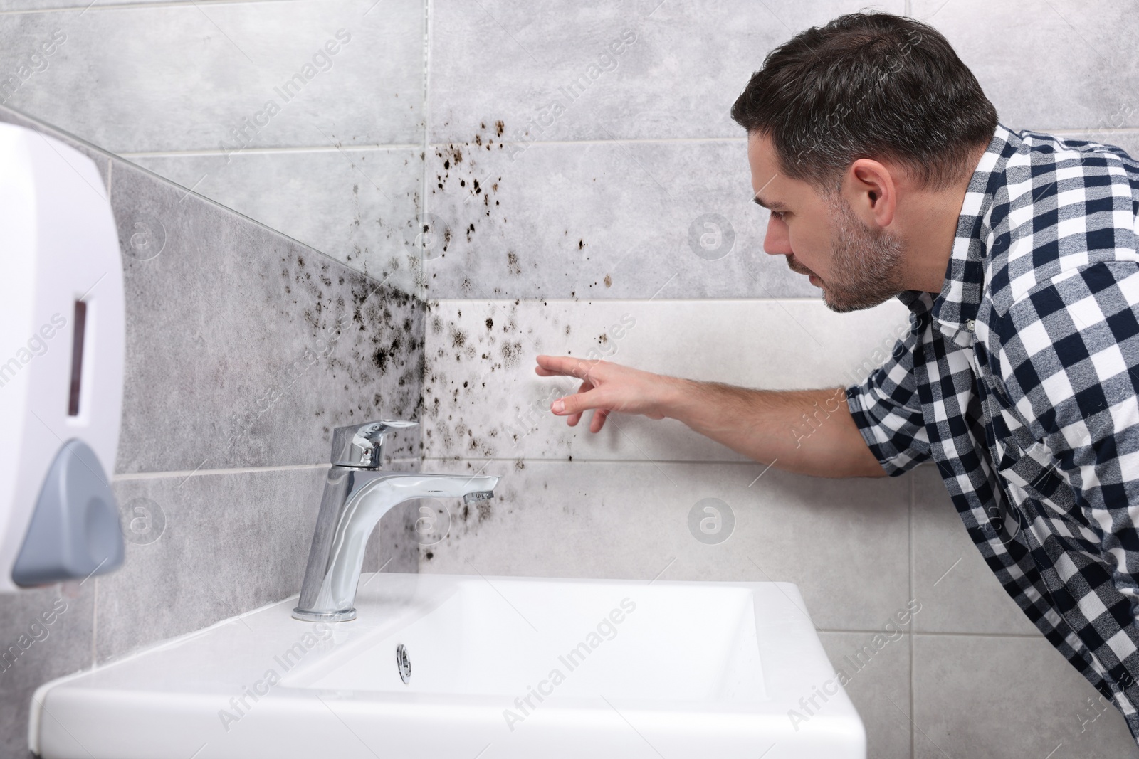 Image of Man looking at affected with mold walls in bathroom