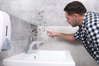 Image of Man looking at affected with mold walls in bathroom