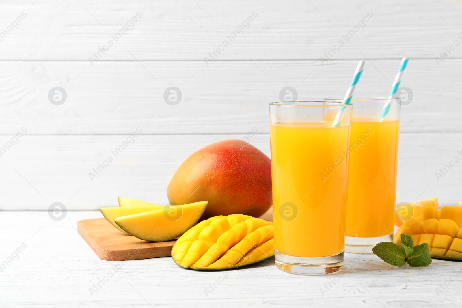 Photo of Tasty mango drink and fresh fruits on wooden table against light background. Space for text