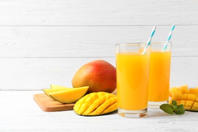 Photo of Tasty mango drink and fresh fruits on wooden table against light background. Space for text