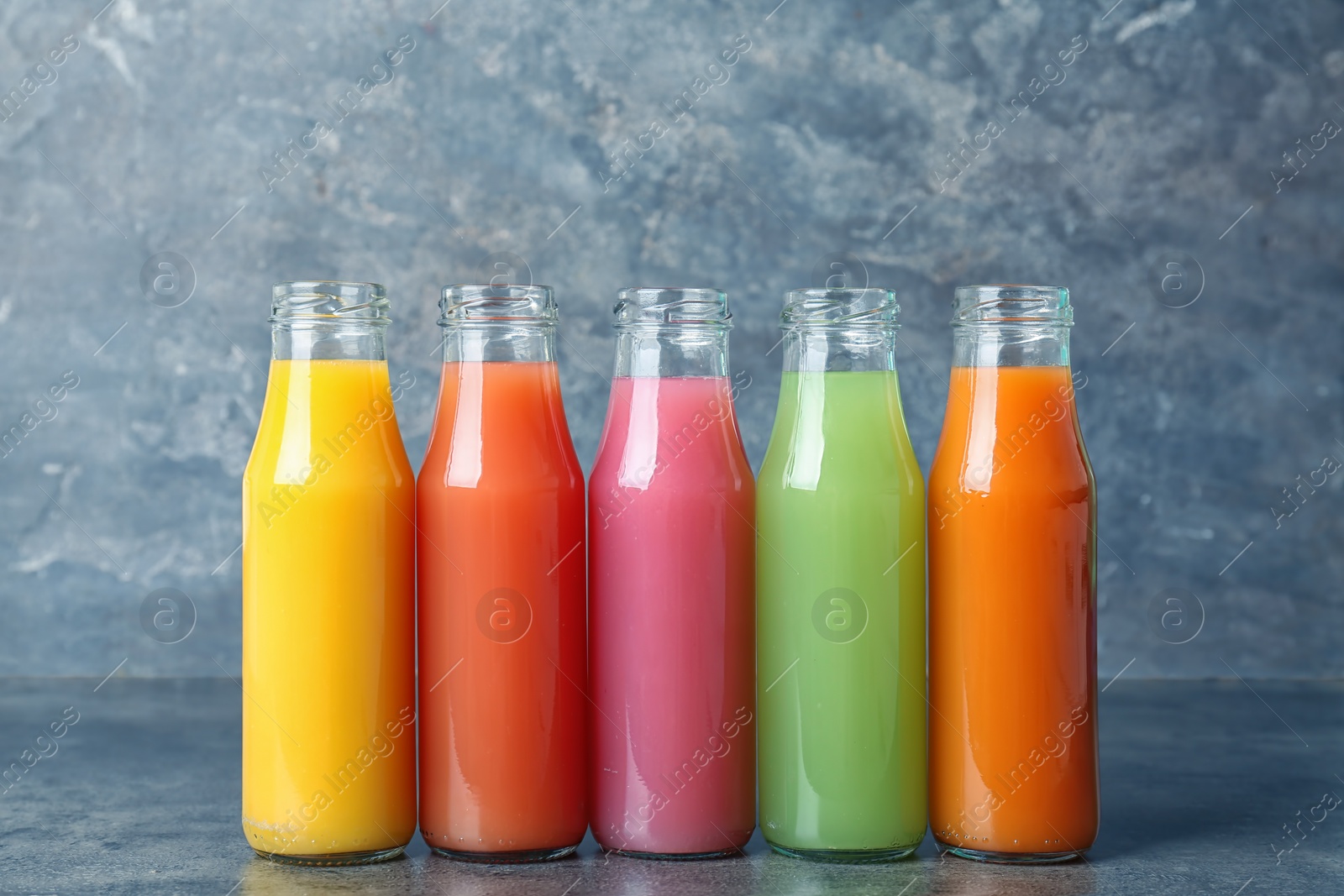 Photo of Bottles of tasty juices on table against grey background