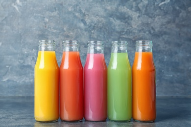 Photo of Bottles of tasty juices on table against grey background