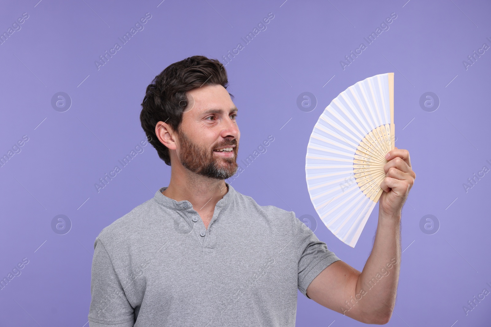 Photo of Happy man holding hand fan on purple background