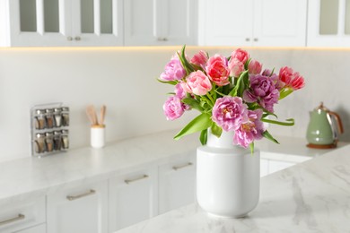 Photo of Beautiful bouquet of colorful tulip flowers on white marble table in kitchen, space for text