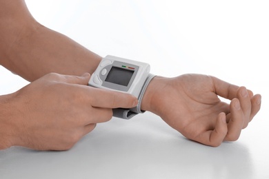 Man checking blood pressure with sphygmomanometer at table against white background, closeup. Cardiology concept