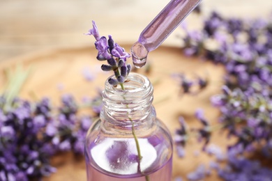 Photo of Natural oil dripping into bottle and lavender flowers on table, closeup. Cosmetic product