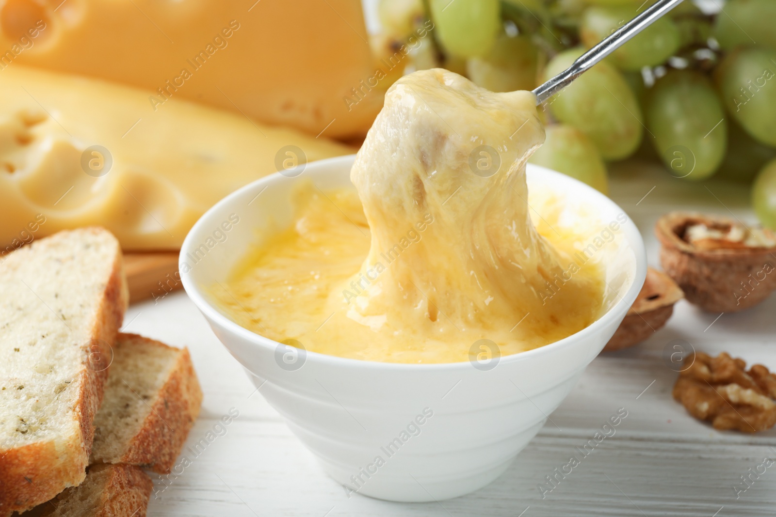 Photo of Dipping piece of bread into bowl with delicious cheese fondue on table