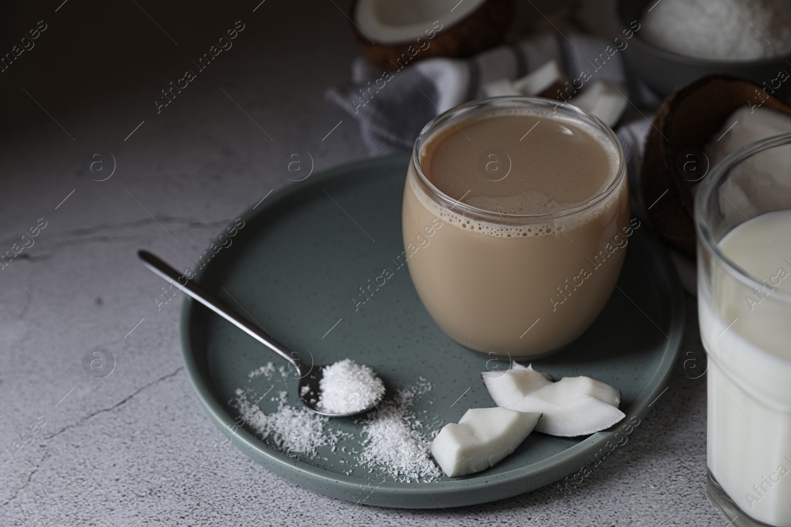 Photo of Glass of coffee with coconut milk, pieces and flakes on light grey table, space for text