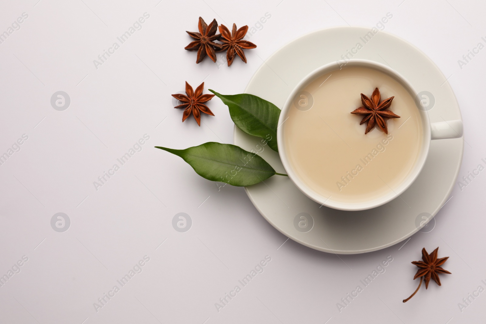 Photo of Cup of tea with milk, anise stars and green leaves on white table, flat lay. Space for text