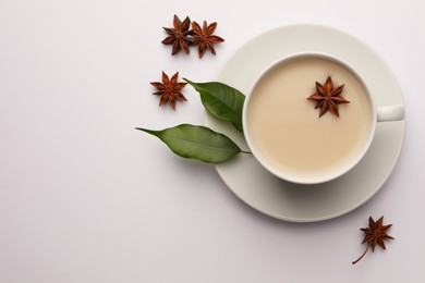 Cup of tea with milk, anise stars and green leaves on white table, flat lay. Space for text