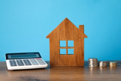 Photo of House model, calculator and stacked coins on wooden table against light blue background