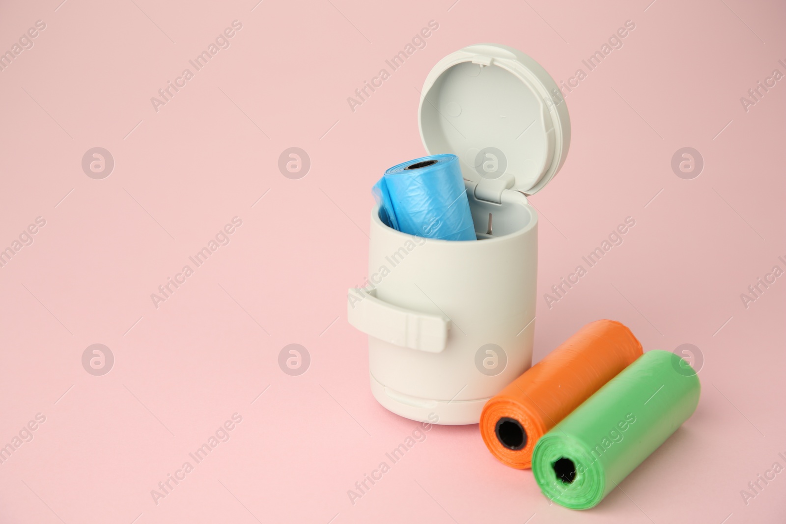 Photo of Dog waste bags and dispenser on pink background. Space for text