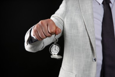 Businessman holding pocket watch on black background, closeup. Time management