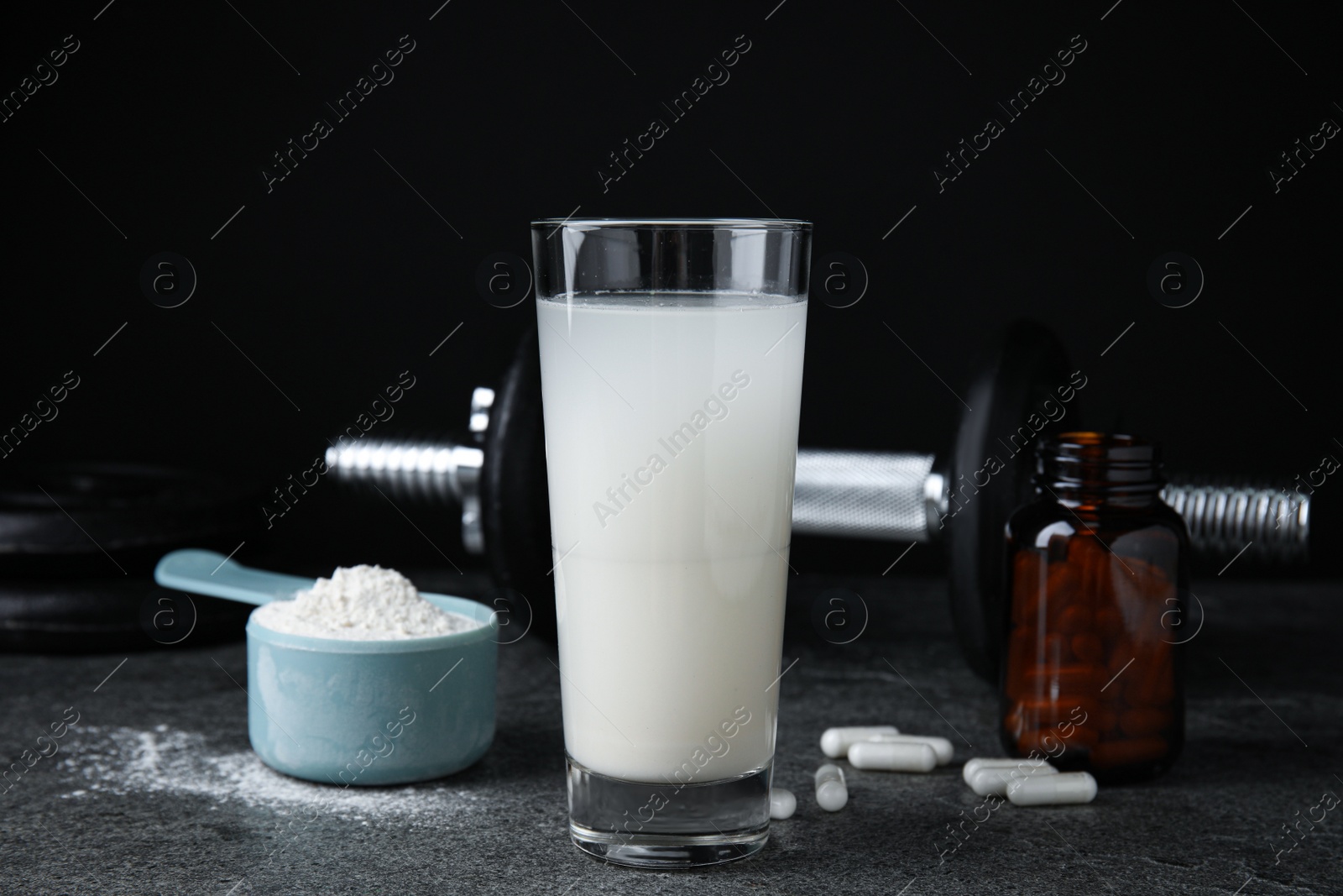 Photo of Amino acid shake, powder, pills and dumbbell on grey table