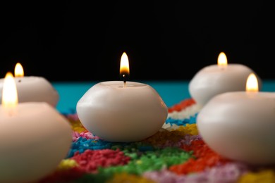 Photo of Diwali celebration. Burning candles and colorful rangoli against black background, closeup