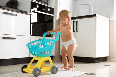 Photo of Cute baby with toy walker in kitchen. Learning to walk