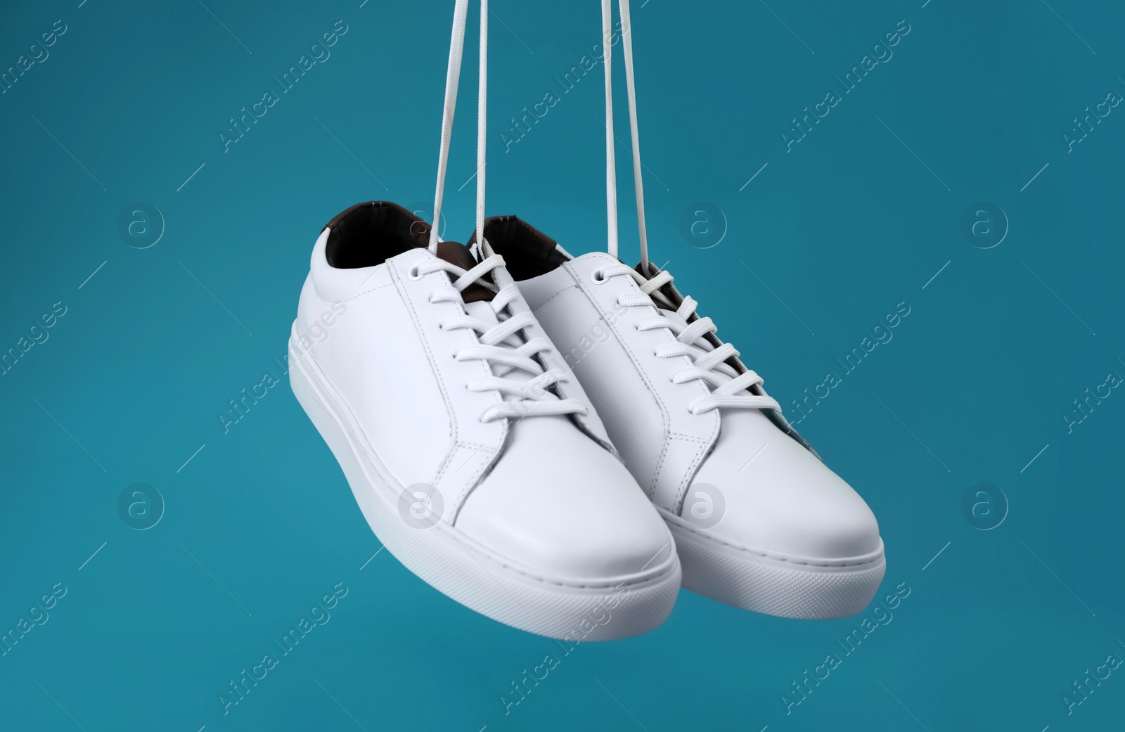 Photo of Pair of stylish sports shoes hanging on blue background