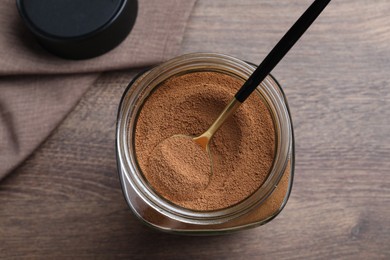 Jar of instant coffee and spoon on wooden table, top view