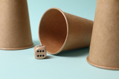 Photo of Three paper cups and dice on light blue background, closeup. Thimblerig game