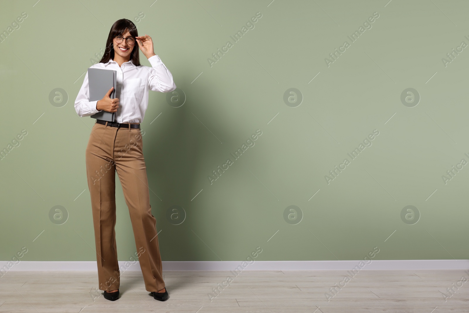 Photo of Happy secretary with folder near light olive wall indoors. Space for text
