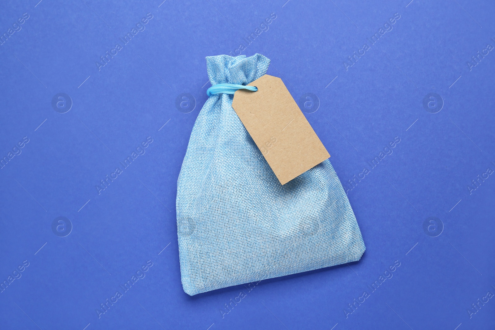 Photo of Color burlap bag with tag on blue background, top view