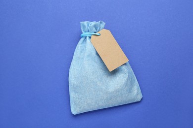 Photo of Color burlap bag with tag on blue background, top view