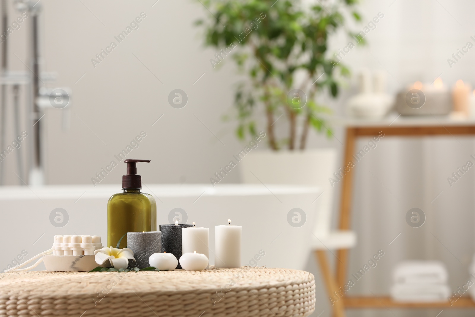 Photo of Spa products, burning candles and plumeria flower on wicker table in bathroom. Space for text