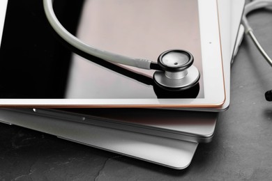 Photo of Stack of electronic devices and stethoscope on black table, closeup